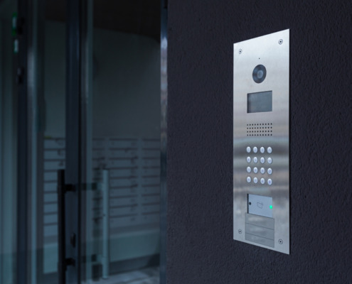 Entrance doorbell in a multi-apartment building, with a video surveillance camera, on a dark wall